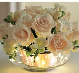 Glass bowl filled with luminous led lights adorned with peach roses